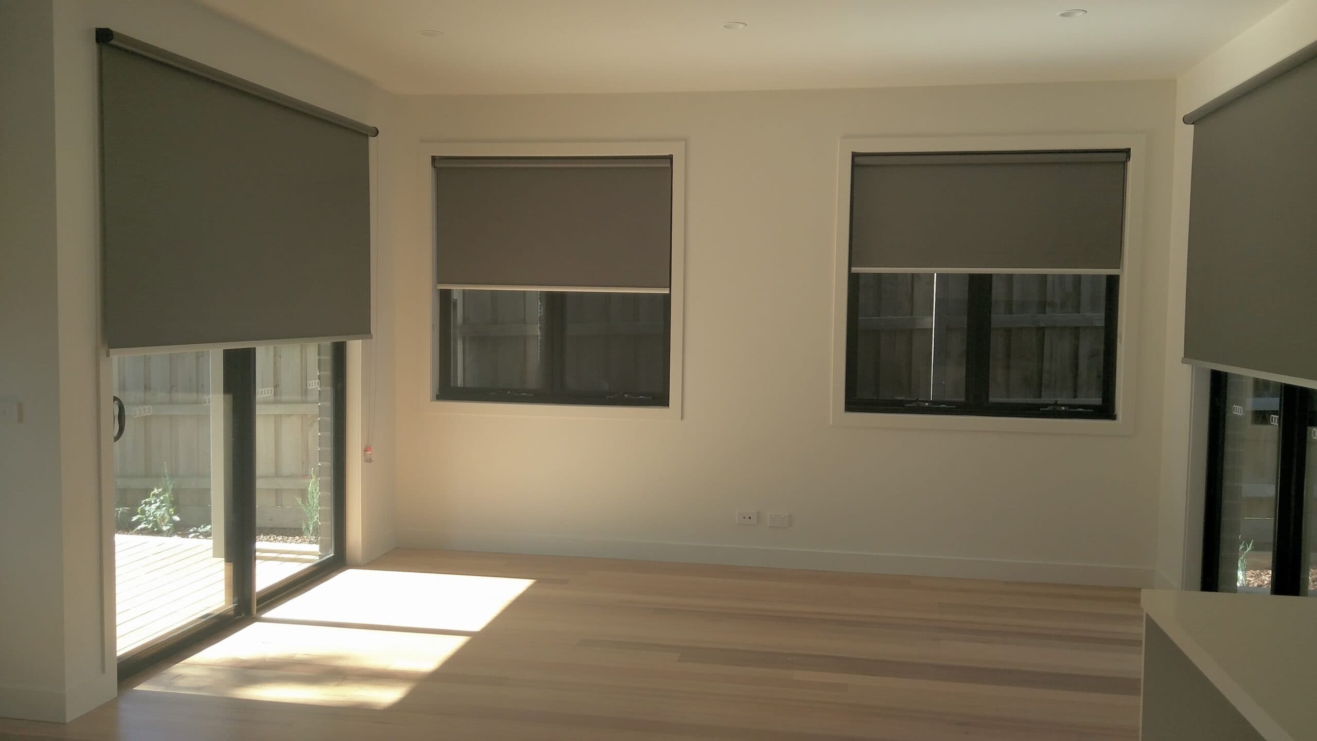 Charcoal roller blinds on three windows and a sliding door in a new living room