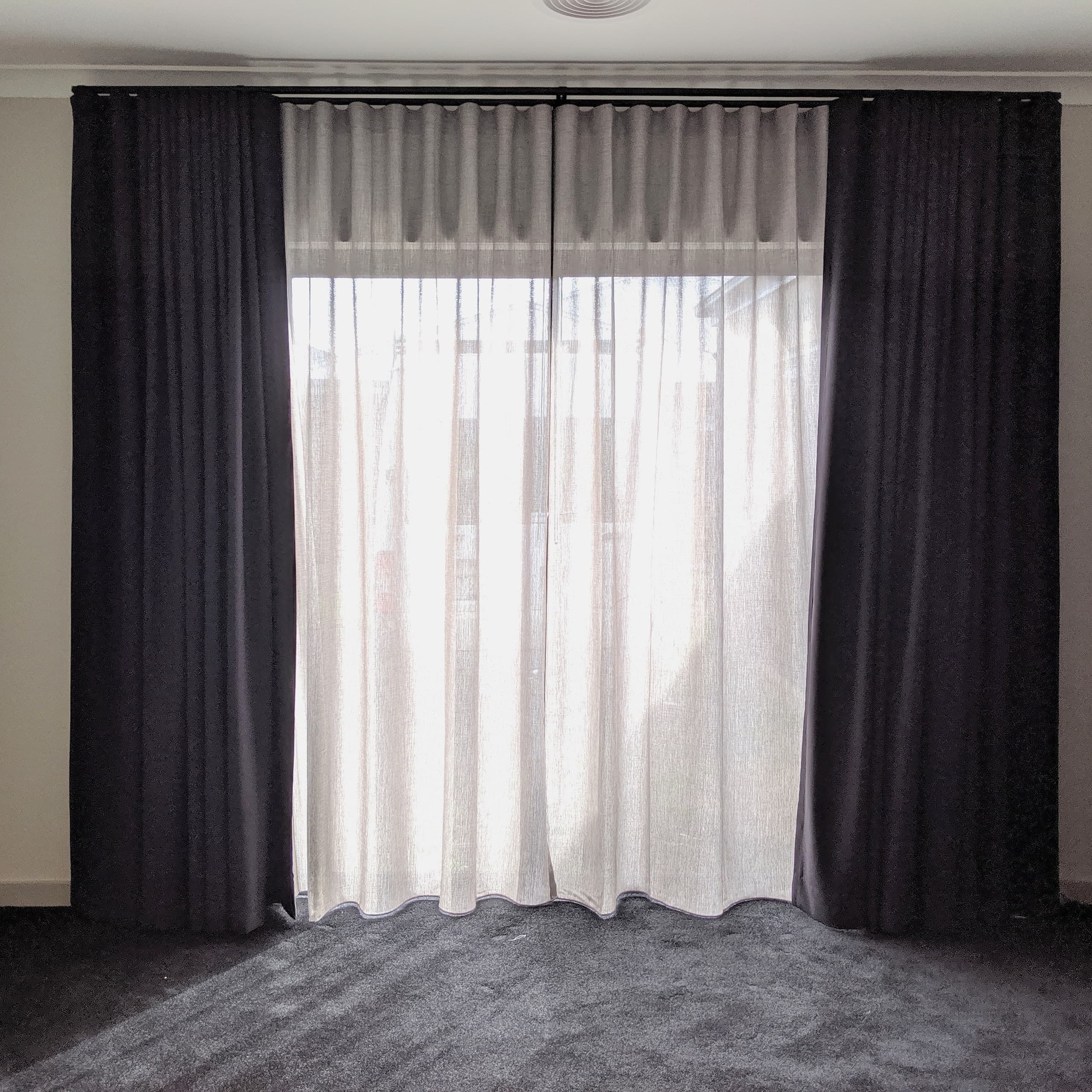 Charcoal blockout curtains layered over a sheer on a double track