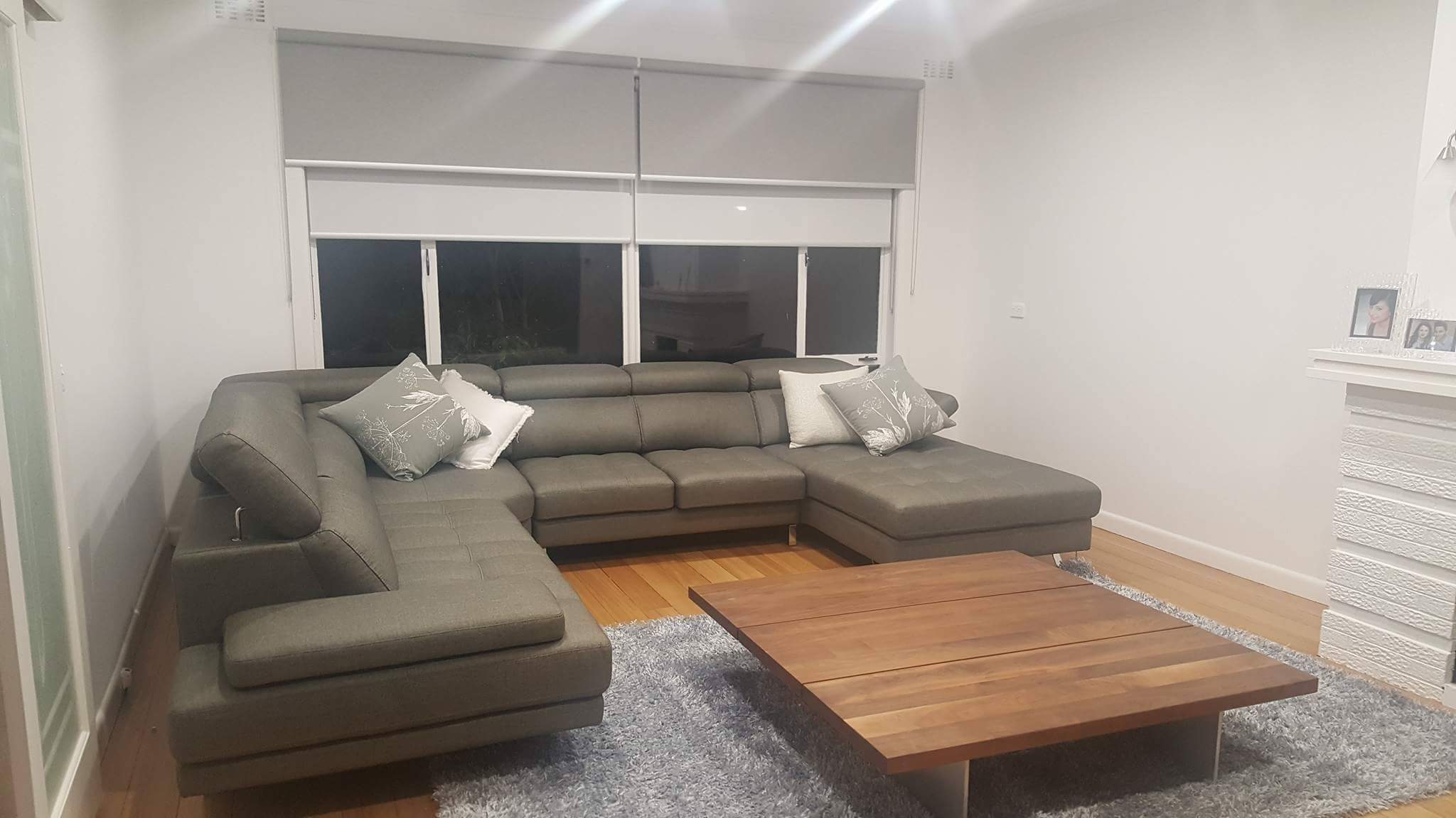 Grey double roller blinds, blockout over sunscreen, on two living room windows at night