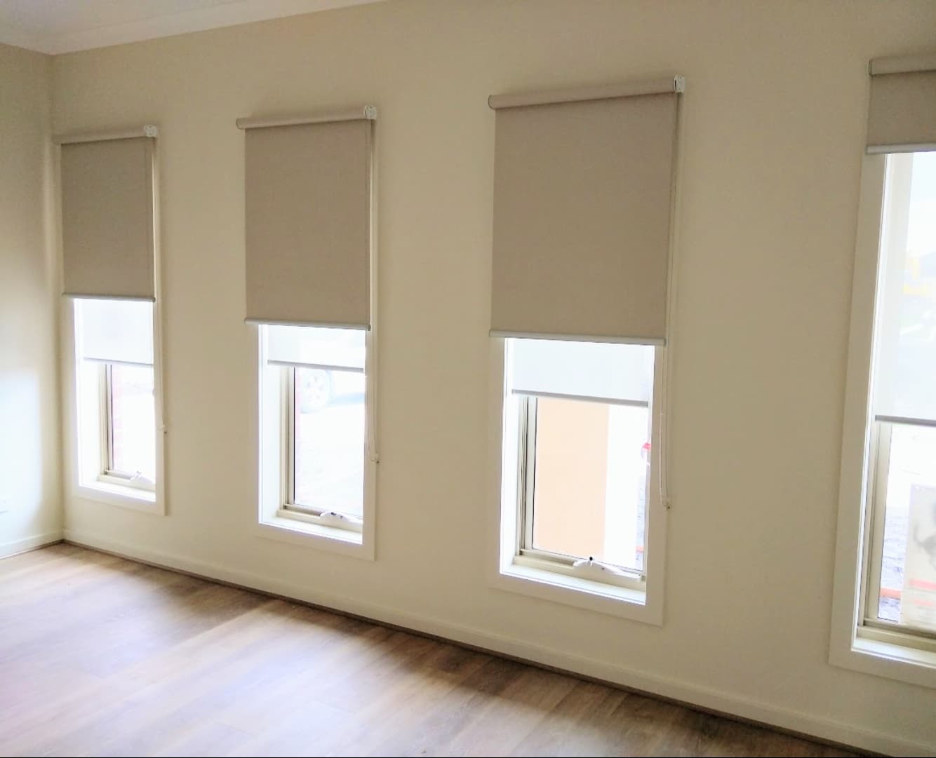 Grey roller blinds on three tall windows above a timber floor