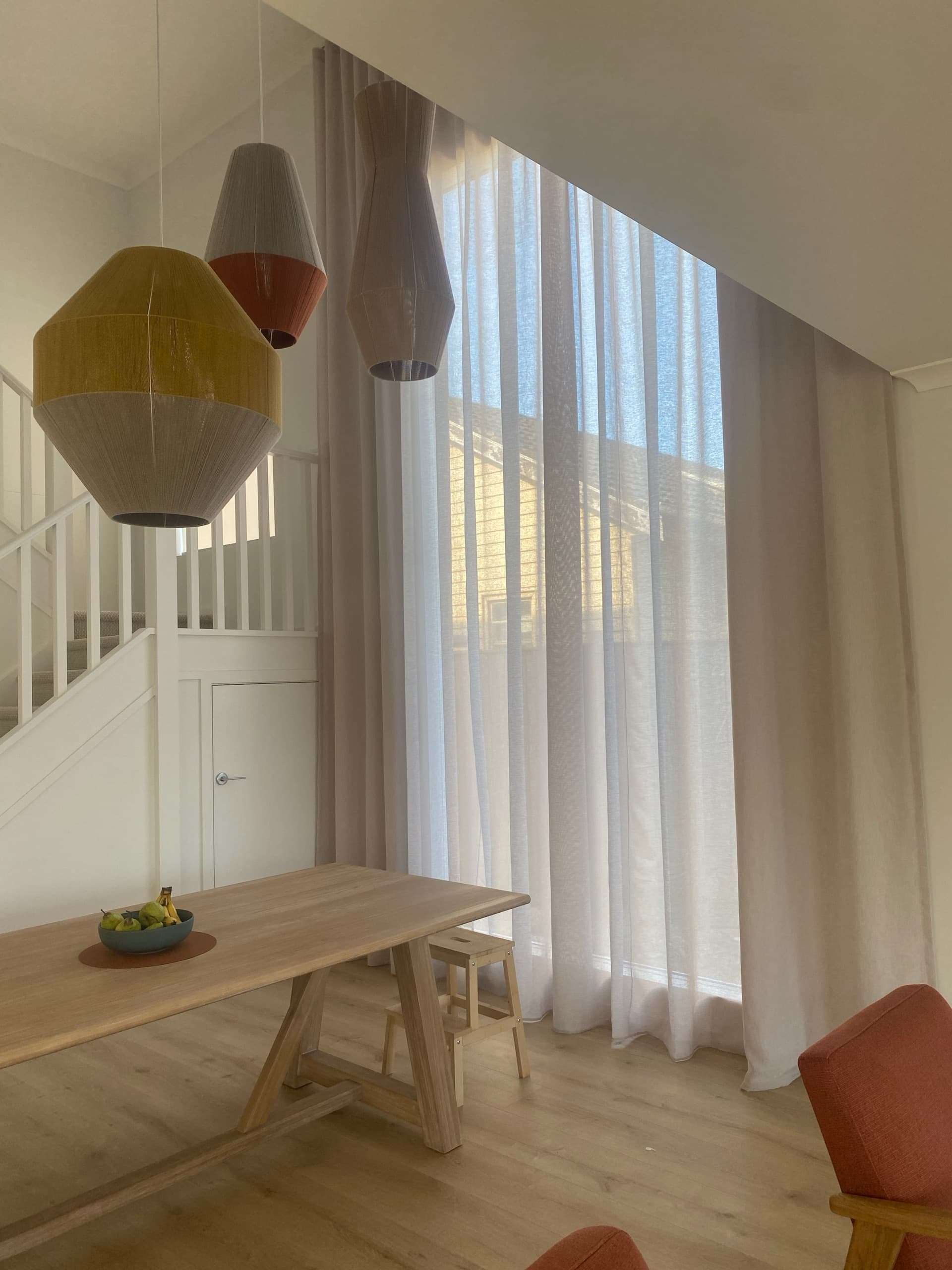 Tall S-fold sheer curtains beside a staircase with pendant lights