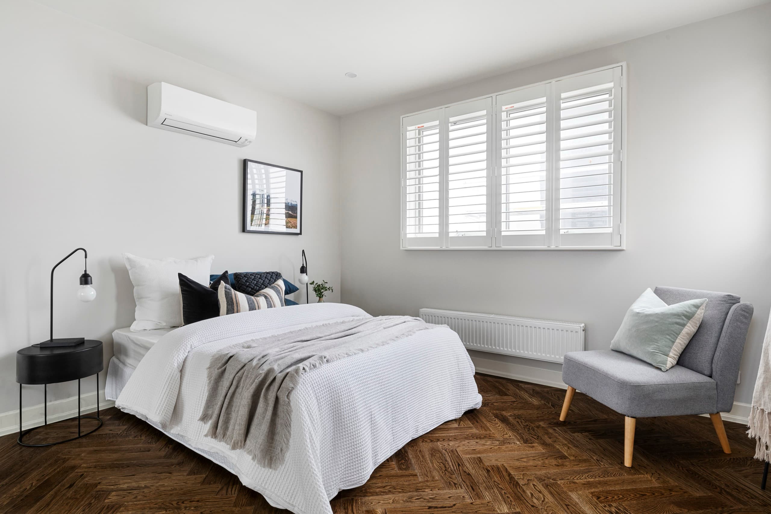 White PVC plantation shutters on a bedroom window with a grey bedhead