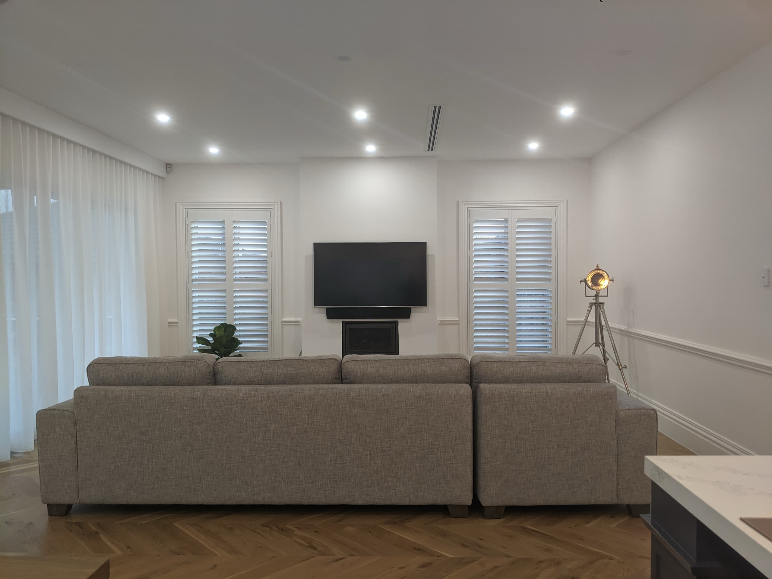 White plantation shutters across a living room window behind a grey sofa