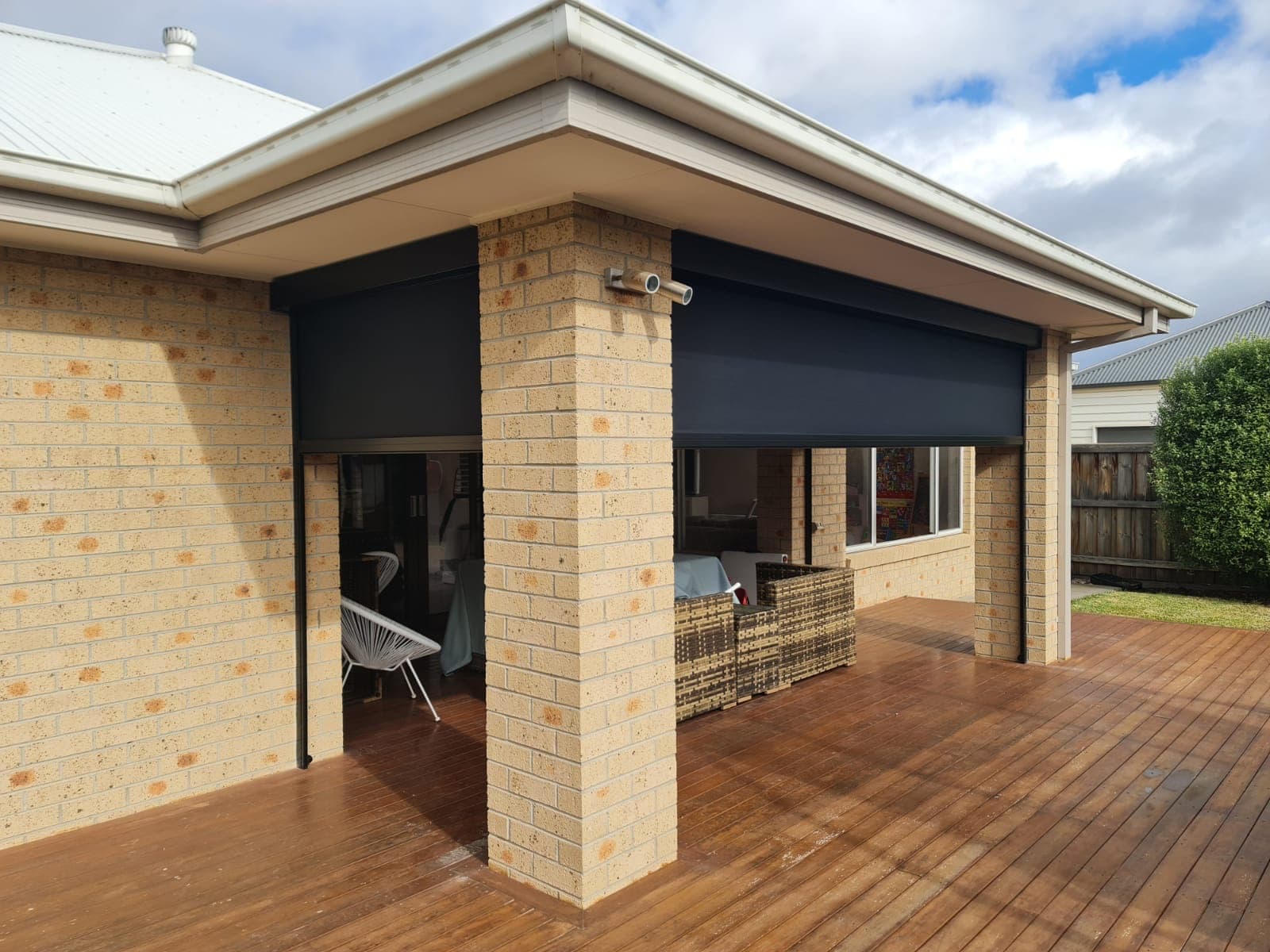 Charcoal zip screen blinds on a brick alfresco, one raised to show the deck
