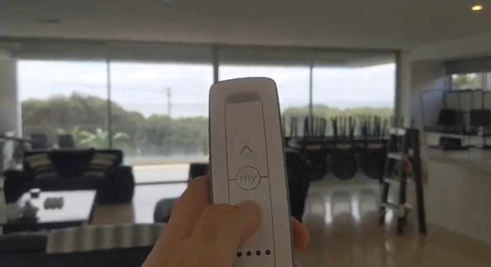 Hand holding a remote control in front of motorised blinds